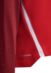 Gros plan sur un tissu rouge avec une insertion blanche et le texte « BEECOOL » imprimé près de l'ourlet, montrant les détails de la couture et de la texture.