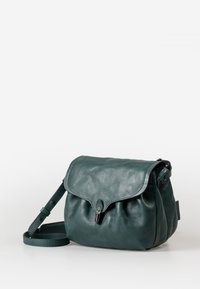Groene leren crossbodytas met een klep sluiting, subtiele textuur, verstelbare schouderband en een metalen sluiting detail. Zacht, rondvormig.
