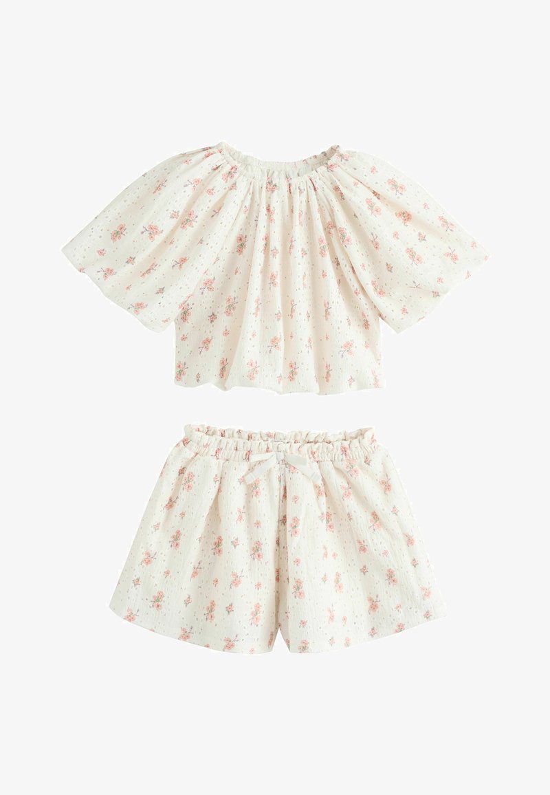 Hvidt todelt børnetøj med pink blomstermønster, der består af en indsamlet off-shoulder top og shorts med elastisk talje og dekorativ sløjfe.