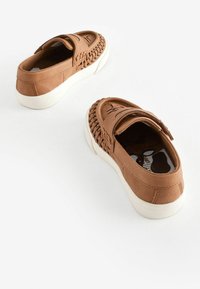 Bruna slip-on skor gjorda av mjukt tyg med en strukturerad vävd detalj längs sidorna och en vit gummisula.
