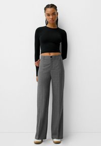 Crop top noir à manches longues associé à un pantalon large à rayures grises, avec une fermeture à boutons et un tissu texturé.