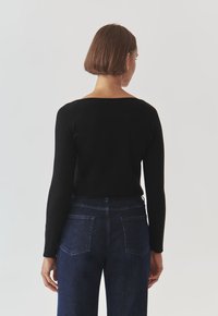 Top negru cu mânecă lungă și gât larg, purtat cu blugi din denim închis la culoare, care au două buzunare la spate și croială dreaptă.