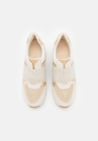 Une paire de baskets beiges et crèmes avec des larges bandes en tissu sur le dessus, des coutures visibles et une doublure intérieure rembourrée, vue de dessus.