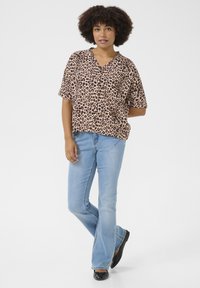 Camicia a maniche corte con stampa leopardata in tessuto leggero, design a scollo a V; abbinata a jeans svasati azzurri chiari e ballerine nere.