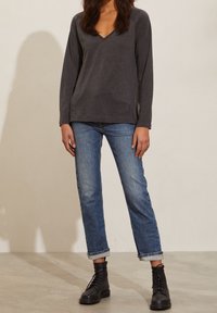 Grå långärmad V-ringad topp i kombination med uppvikta blå jeans och svarta snörda militärstövlar, med en avslappnad passform och mjuk textur.