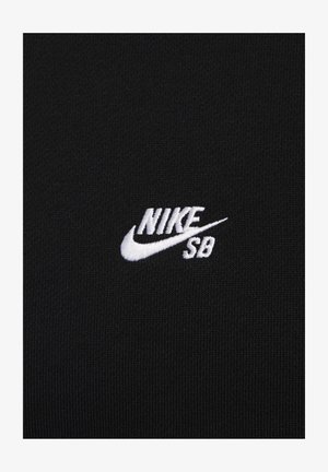 Melns audums ar gludu tekstūru, kurā ir balts izšūts Nike SB logo klasiskajā fontā. Vienkāršs un mūsdienīgs dizains.