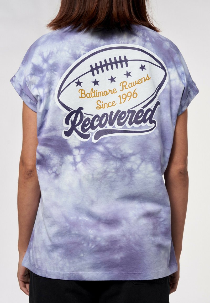 Lila tie-dye T-shirt med rullade korta ärmar. Har en fotbollsgraphic med "Baltimore Ravens Sedan 1996" och texten "Återvunnen".
