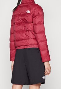 Persona que lleva una chaqueta acolchada roja y pantalones cortos negros, ambos con el logo de The North Face, vistos desde atrás.