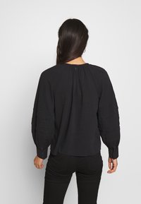 Svart blus med vida ärmar och texturerad detaljer, med en knappstängning bak och en lös passform.