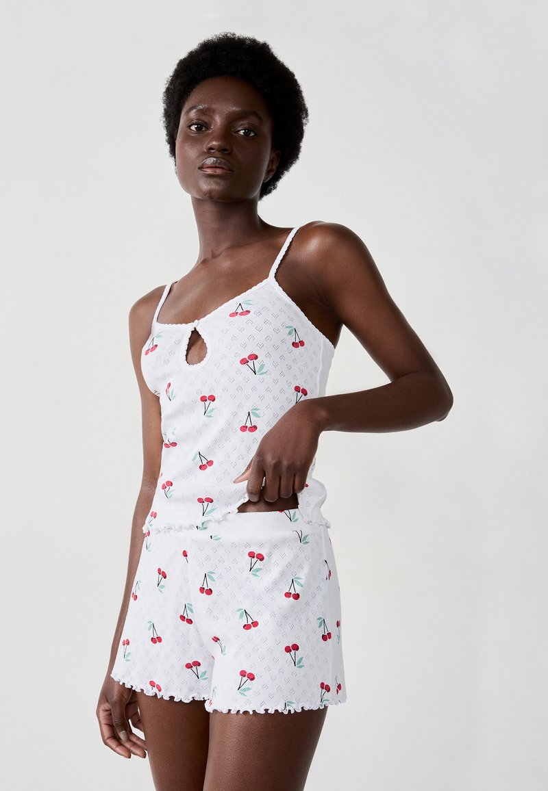 Set da notte bianco composto da un top senza maniche con dettaglio a chiave e stampa di ciliegie, abbinato a pantaloni corti con bordi arricciati.