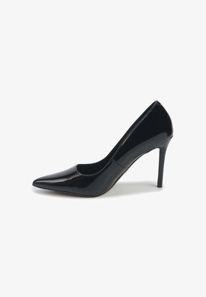 Escarpin en cuir verni noir à talon haut avec un bout pointu et un talon aiguille fin sur fond blanc.