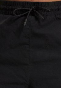Schwarze Shorts mit einem elastischen Bund und Kordelzug. Der Stoff hat eine dezente Karomusterung und eine glatte Oberfläche.