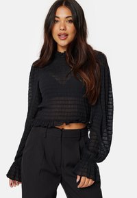 Top nero, trasparente, a maniche lunghe con tessuto testurizzato, orlo a volant e maniche a campana, abbinato a pantaloni neri a vita alta.