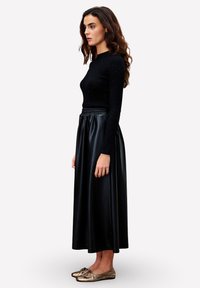 Zwarte geribbelde lange mouw top met subtiele embellissements, gecombineerd met een zwarte kunstlederen lange rok en metalen platte schoenen.