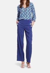 Blå mönstrad blus med långa ärmar, i kombination med enfärgade blå vida byxor med två vita knappdetaljer vid framfickorna.