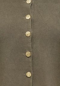 Gros plan sur un tissu marron tricoté avec cinq boutons ronds dorés texturés alignés verticalement.