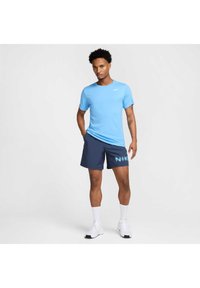 Jasnoniebieska koszulka sportowa z krótkim rękawem z białym logo, w zestawie z granatowymi szortami z jasnoniebieską grafiką. Białe skarpetki i tenisówki.