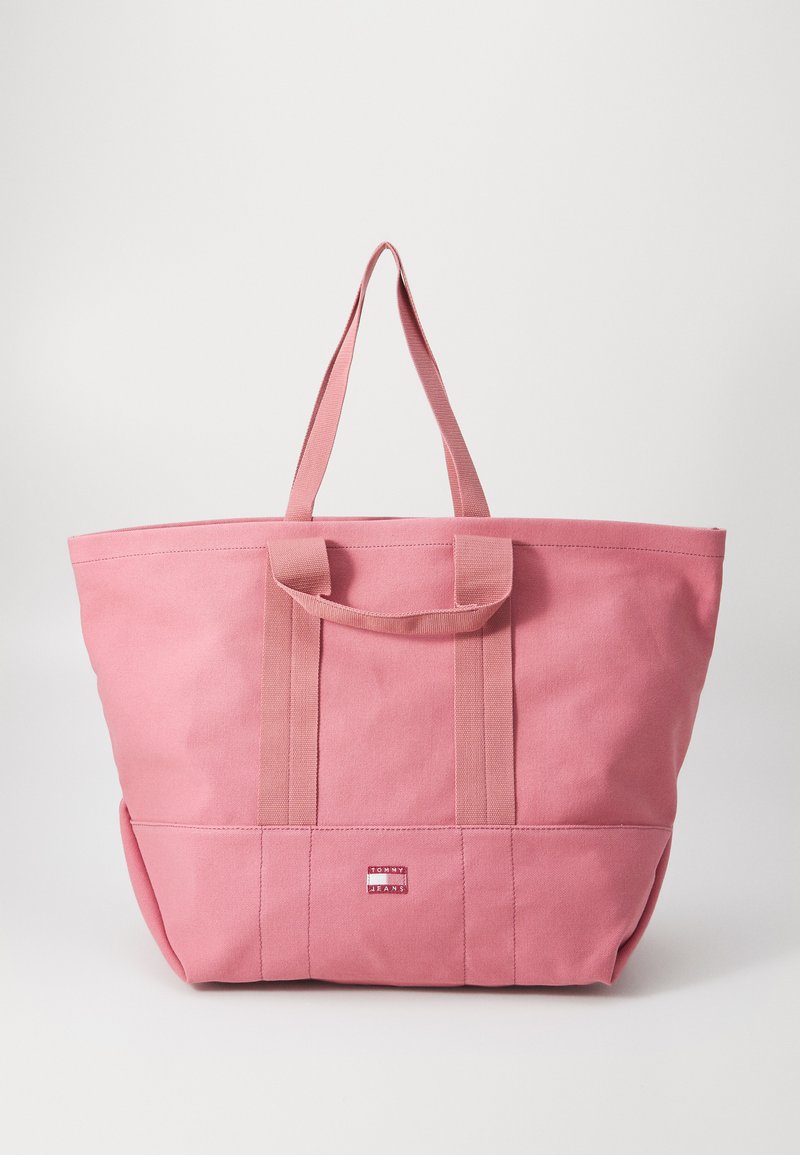 Rosa Canvas-Shopper-Tasche mit doppelten oberen Griffen, robustem Design und einem kleinen Markenpatch nahe dem Boden. Glatte Textur mit geräumigem Innenraum.