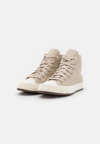 Beige high-top sneakers made of canvas with white rubber toe caps and soles, featuring metal eyelets and textured laces.