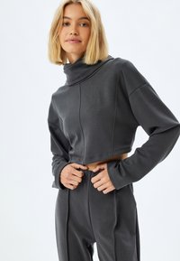 Czarnoszary, skrócony sweatshirt z wysokim kołnierzem, długimi rękawami i teksturowanym materiałem. W zestawieniu z pasującymi spodniami o wysokim stanie.