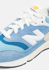 Sneaker in suede blu chiaro e turchese con logo bianco, dettagli in rete e lacci crema. Suola ammortizzata con finitura testurizzata.
