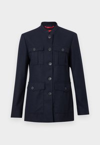Sötétkék dzseki strukturált anyagból, álló gallérral, hat elülső zsebbel és gombokkal a frontrész zárásán.