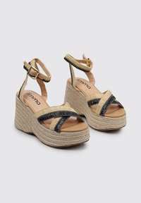 Sandalias de cuña con plataforma de yute trenzado, con parte superior beige y tiras de acento negras, y cierre de hebilla para un ajuste seguro.