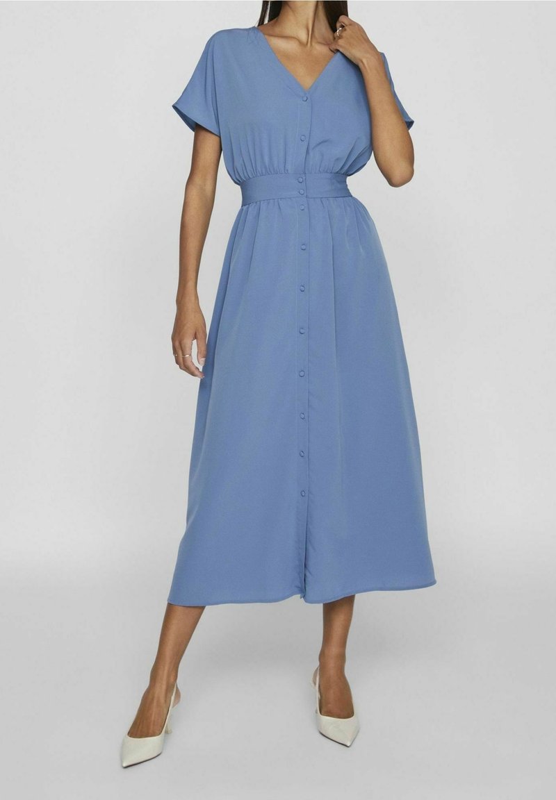 Sininen midi-mekko, jossa on V-pääntie, lyhyet hihat, joustava vyötärö ja etupuolella nappikiinnitys. Sujuva kangas, jossa on kevyt rakenne.