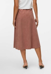 Jupe midi rose poussiéreux avec une texture lisse, une taille élastique et des lignes verticales subtiles. Modèle portant des sandales à talons ouverts.
