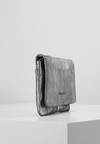 Borsa clutch metallizzata argento con una texture morbida, dotata di patta pieghevole e un semplice logo sul davanti. Design compatto e rettangolare.