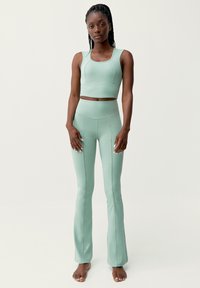 Sada aktivního oblečení v mátově zelené barvě obsahující vypasovaný crop top se zaobleným výstřihem a odpovídající vysoké legíny se zvonovými nohavicemi a švy.