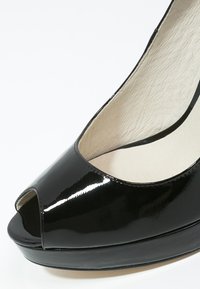 Escarpin en cuir verni noir ouvert, avec une surface lisse, un design arrondi et une semelle compensée pour plus de hauteur et de stabilité.