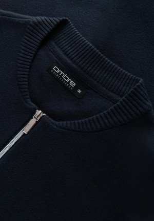 Dunkelblauer Pullover mit ribbeltem Rundhalsausschnitt und Reißverschluss vorne. Verfügt über eine glatte Textur und ein markiertes Etikett im Kragen.
