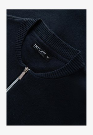 Dunkelblauer Pullover mit ribbeltem Rundhalsausschnitt und Reißverschluss vorne. Verfügt über eine glatte Textur und ein markiertes Etikett im Kragen.