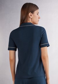 Marinblå kortärmad polo med krage, med vit pipning längs kragen och ärmarna. Mjuk och slät textur.