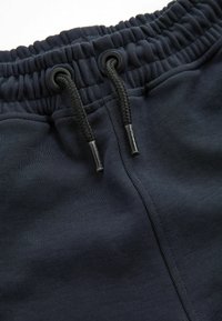 Mörkblå sweatpants har ett elastiskt midjeband, snörning och en slät yta. Inga synliga mönster eller hårdvarudetaljer visas.