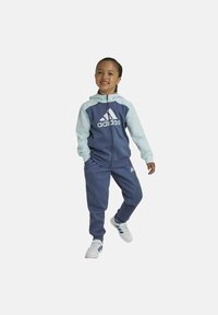 Chándal juvenil de Adidas en azul marino y celeste, que incluye sudadera con cremallera, logo blanco y pantalones de chándal a juego con puños elásticos.
