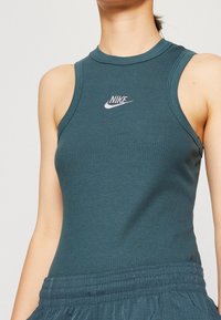 Close-up of person wearing teal ribbed sleeveless Nike top and matching textured pants, showing upper torso and logo on chest.