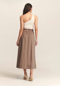 Top de tirantes blanco acanalado con un solo tirante, combinado con una falda beige hasta los tobillos que cuenta con una cinturilla elástica y una textura suave.
