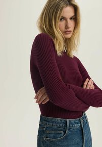 Bordowy, prążkowany top z długim rękawem o dopasowanym kroju, połączony z niebieskimi dżinsami o wysokim stanie z klasycznym pięciopocketowym stylem i teksturą denimu.