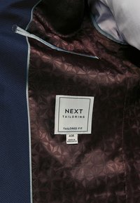 Maßgeschneiderte Jacke mit einer strukturierten navyfarbenen Außenseite und gefüttertem burgunderfarbenem Innenfutter. Das Etikett zeigt die Marke "NEXT", Größe 40R und hergestellt in Bangladesch.