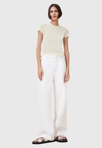 T-shirt aderente di un delicato giallo chiaro, realizzato in morbido tessuto, abbinato a jeans bianchi larghi a vita alta. Gli accessori includono sandali flat con dettagli in argento.