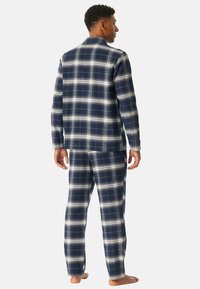 Pijamas de franela azul marino con un patrón de cuadros blancos, que incluyen una camisa con cuello y pantalones con cintura elástica. Textura suave, mangas largas.