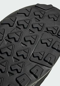 Čierna gumová podrážka s hlbokými, ostrými výstupkami pre trakciu. Má textúrovaný povrch a hexagonálny vzor pre lepšiu priľnavosť.