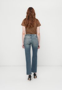 Un haut marron à manches courtes et un jean bleu taille moyenne avec une coupe droite, arborant un design classique à cinq poches et une légère décoloration. Des escarpins noirs.