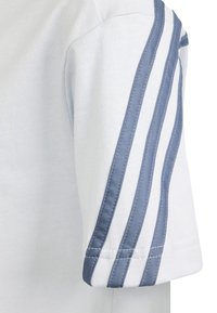 Biała rękaw bluzki z trzema równoległymi niebieskimi paskami materiału biegnącymi od ramienia do mankietu.
