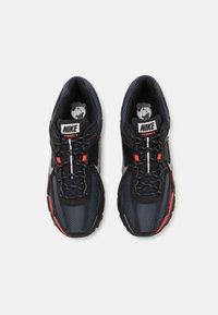 Zapatillas Nike Vomero 5 negras con parte superior de malla y sintético, acentos reflectantes, detalles rojos y suela de goma. Diseño con cordones.
