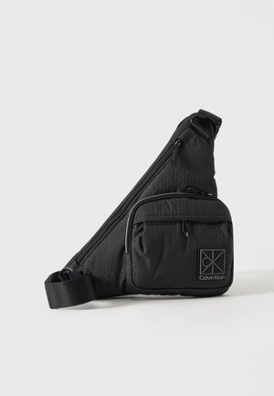 Czarna torebka Calvin Klein na ramię z regulowanym paskiem, przednią kieszenią na zamek i subtelnym wzorem logo na jednolitym tle.