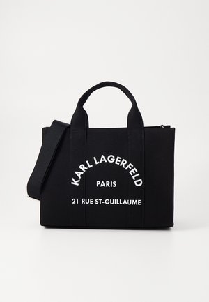 Schwarze rechteckige Tragetasche mit kurzen Griffen und verstellbarem Schulterriemen, weißer Schriftzug "Karl Lagerfeld Paris 21 Rue St-Guillaume" auf der Vorderseite.