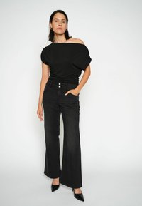 Top nero off-the-shoulder abbinato a jeans neri a vita alta e a gamba larga. Caratteristiche notevoli includono tre bottoni frontali e una texture denim liscia.